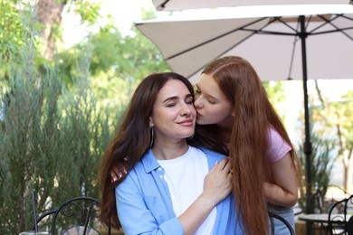 Photo of Teenage daughter kissing her mother in outdoor cafe