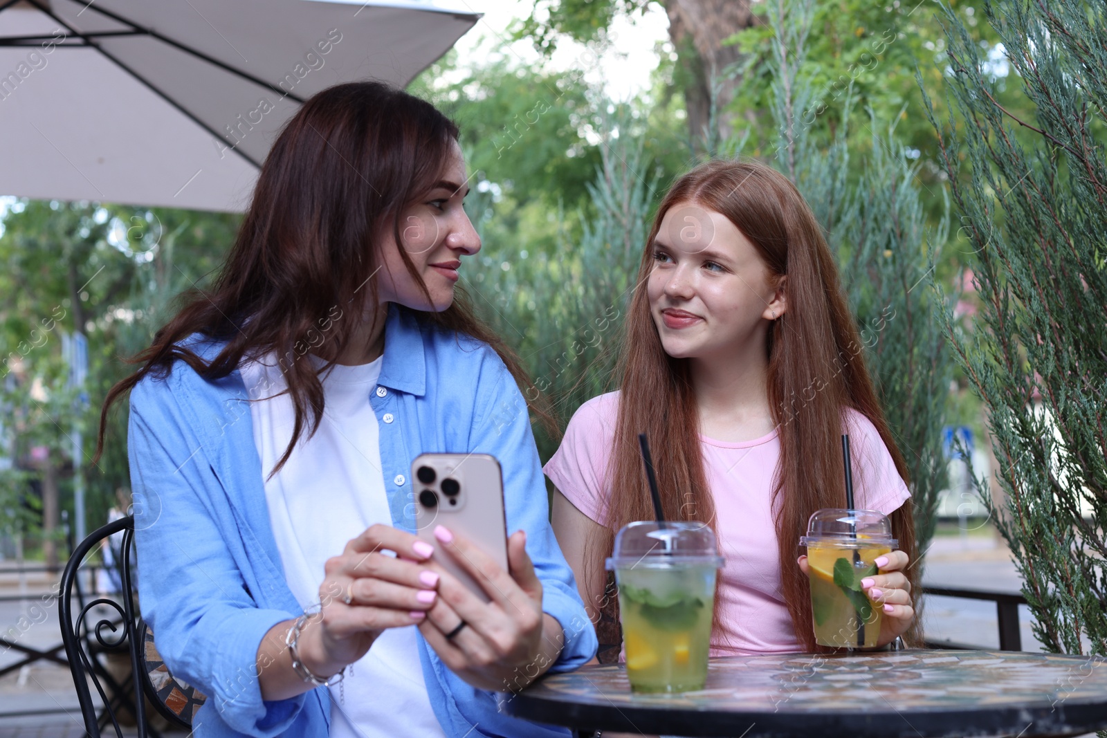 Photo of Beautiful mother and her teenage daughter spending time together with smartphone in outdoor cafe