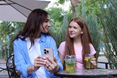 Photo of Beautiful mother and her teenage daughter spending time together with smartphone in outdoor cafe