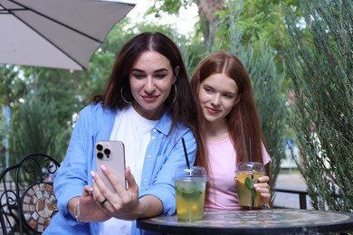 Photo of Beautiful mother and her teenage daughter taking selfie in outdoor cafe