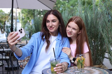 Photo of Beautiful mother and her teenage daughter taking selfie in outdoor cafe