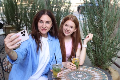 Photo of Beautiful mother and her teenage daughter taking selfie in outdoor cafe