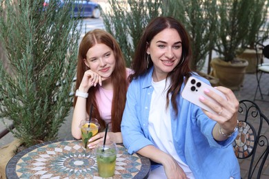 Photo of Beautiful mother and her teenage daughter taking selfie in outdoor cafe