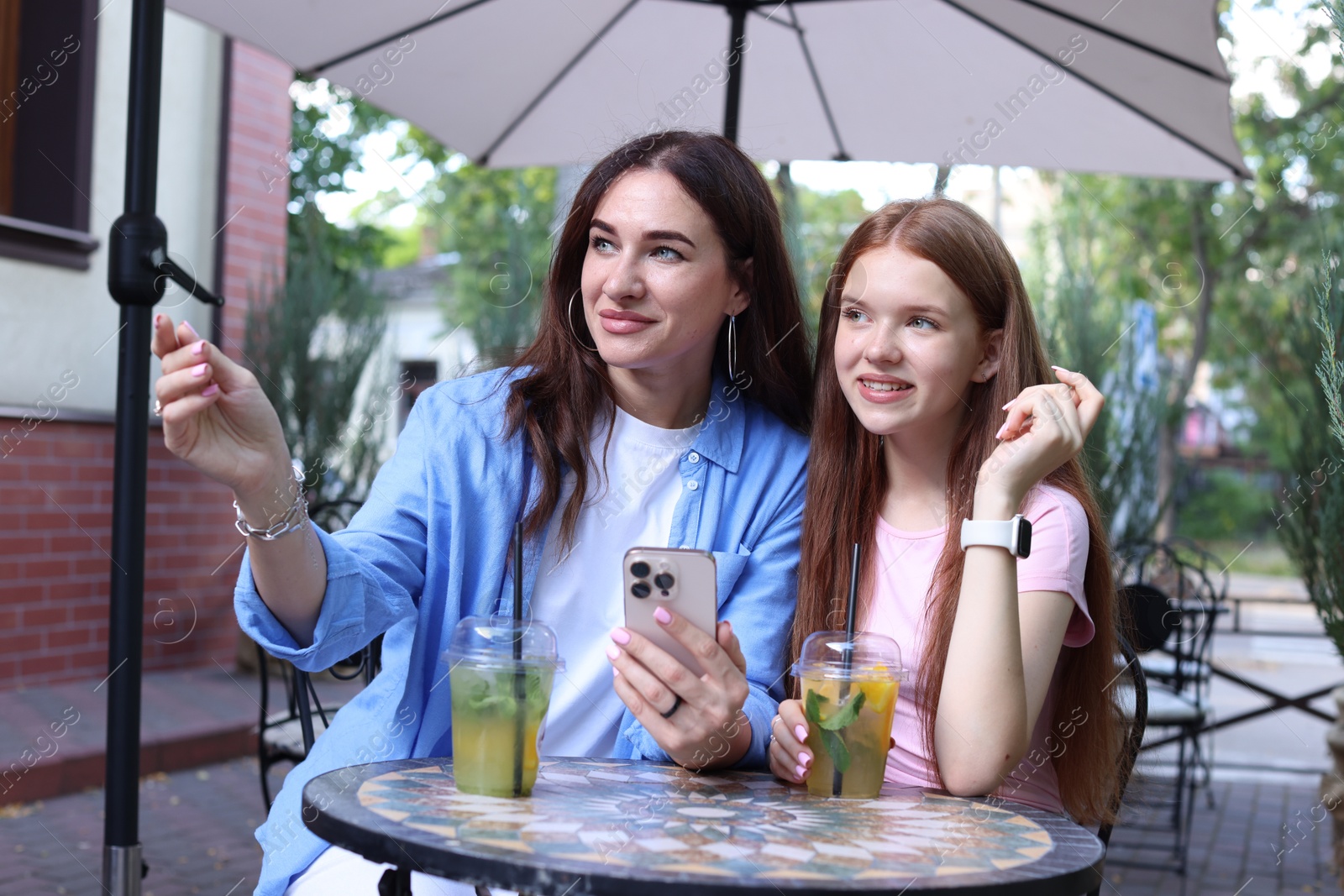 Photo of Beautiful mother and her teenage daughter spending time together in outdoor cafe