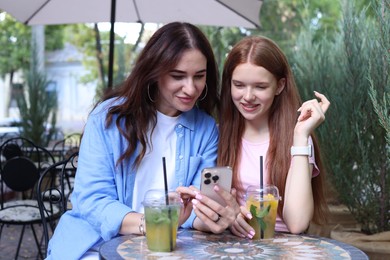 Photo of Beautiful mother and her teenage daughter spending time together with smartphone in outdoor cafe
