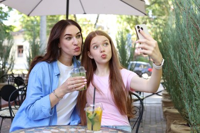 Photo of Beautiful mother and her teenage daughter taking selfie in outdoor cafe