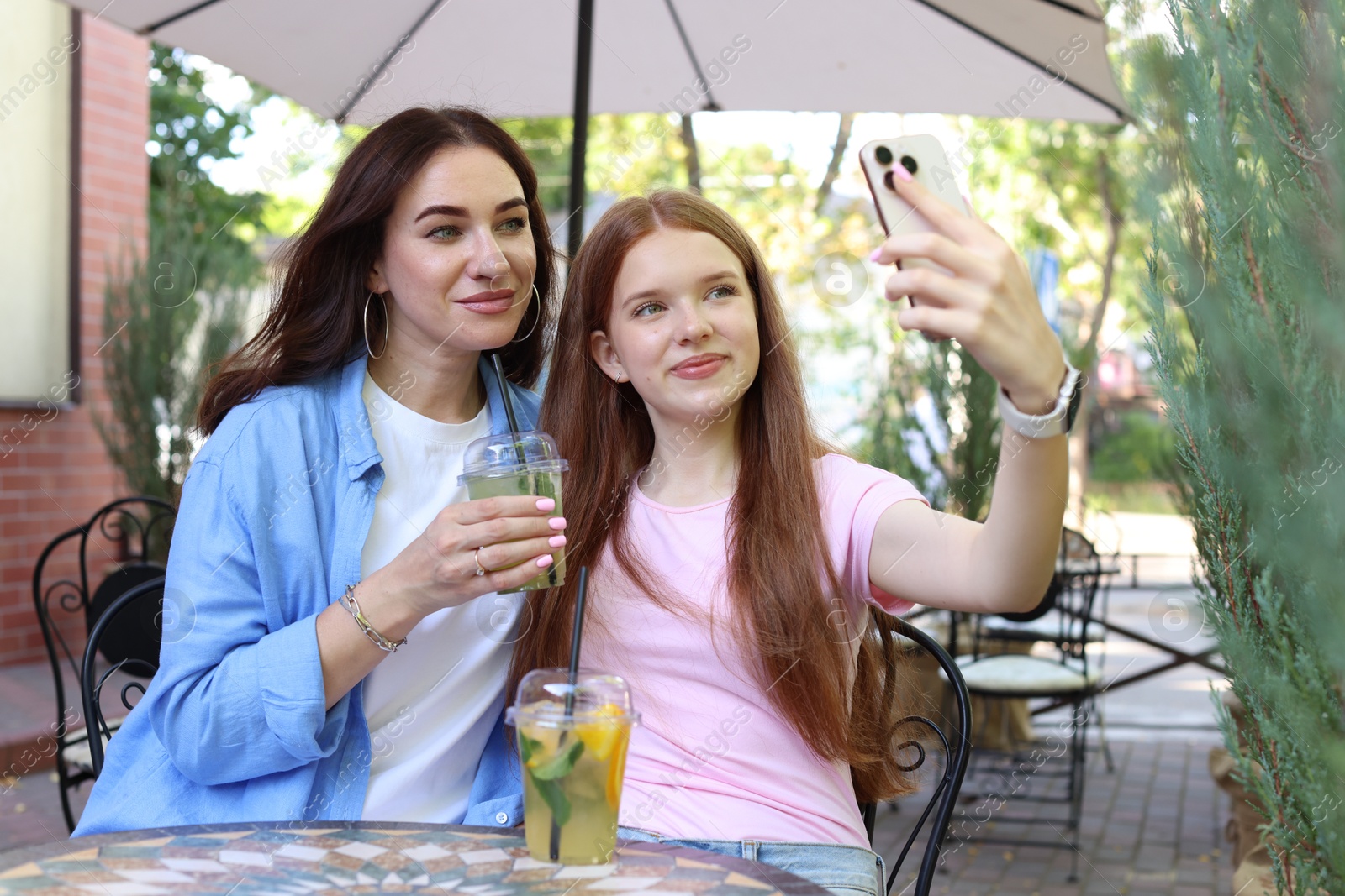 Photo of Beautiful mother and her teenage daughter taking selfie in outdoor cafe