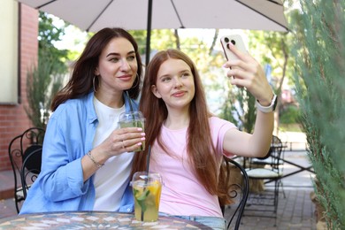 Photo of Beautiful mother and her teenage daughter taking selfie in outdoor cafe