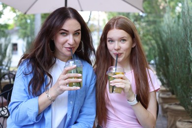 Photo of Portrait of beautiful mother and her teenage daughter with refreshing drinks in outdoor cafe
