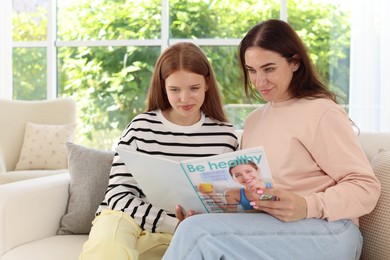 Photo of Mother and her teenage daughter reading magazine together at home
