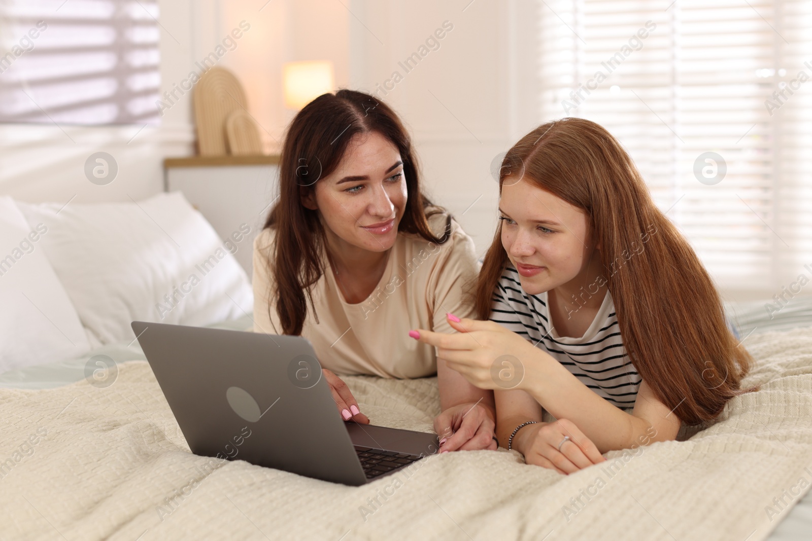 Photo of Mother and her teenage daughter with laptop spending time together on bed at home