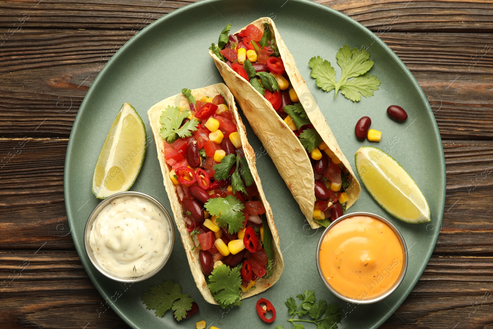 Photo of Tasty vegetarian tacos served with sauces on wooden table, top view