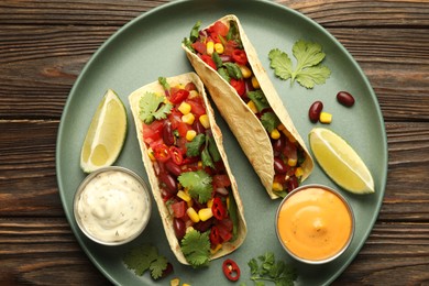 Photo of Tasty vegetarian tacos served with sauces on wooden table, top view