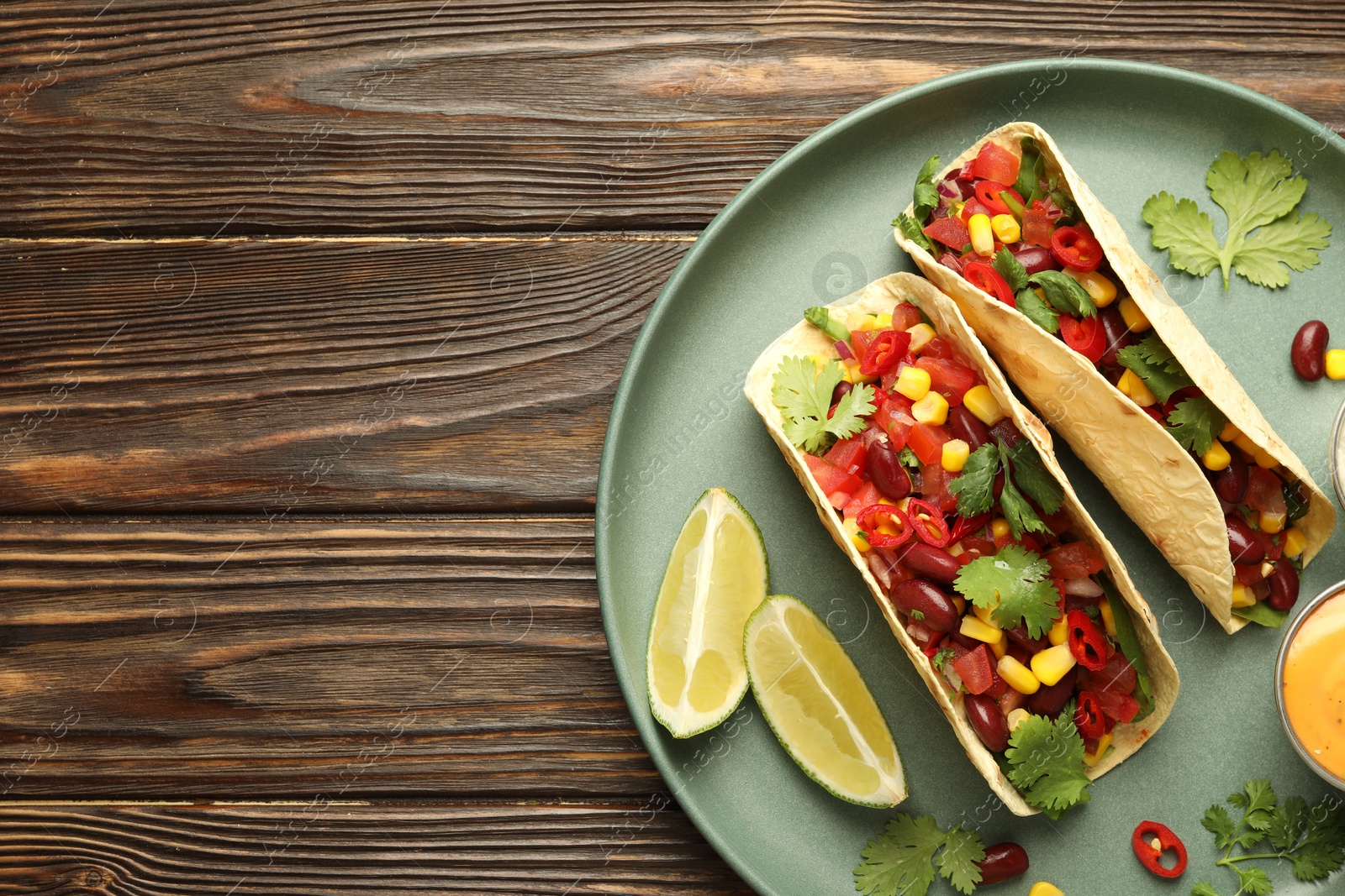 Photo of Tasty vegetarian tacos served on wooden table, top view. Space for text