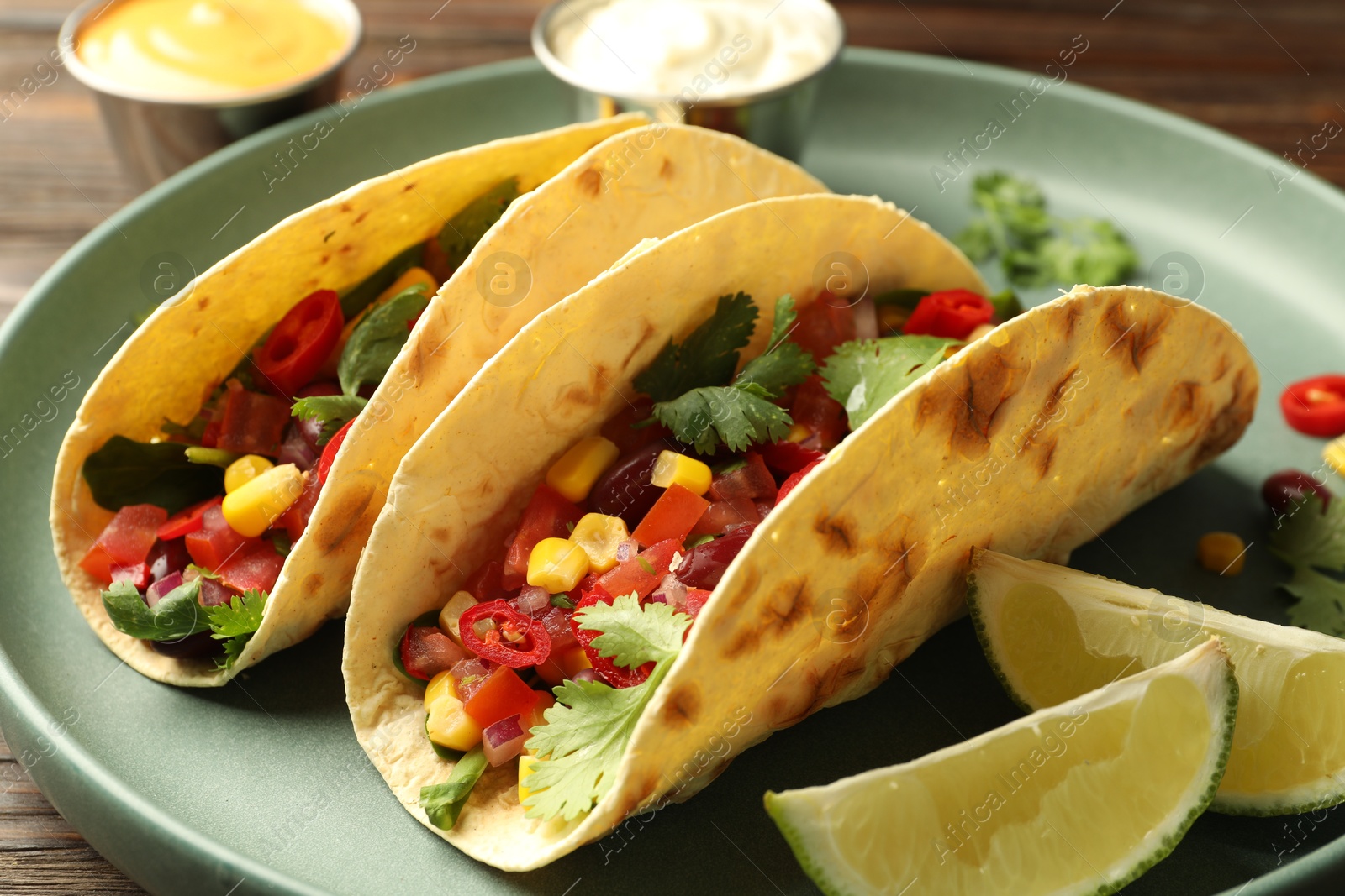 Photo of Tasty vegetarian tacos served with sauces on table, closeup