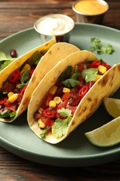Photo of Tasty vegetarian tacos served with sauces on wooden table, closeup