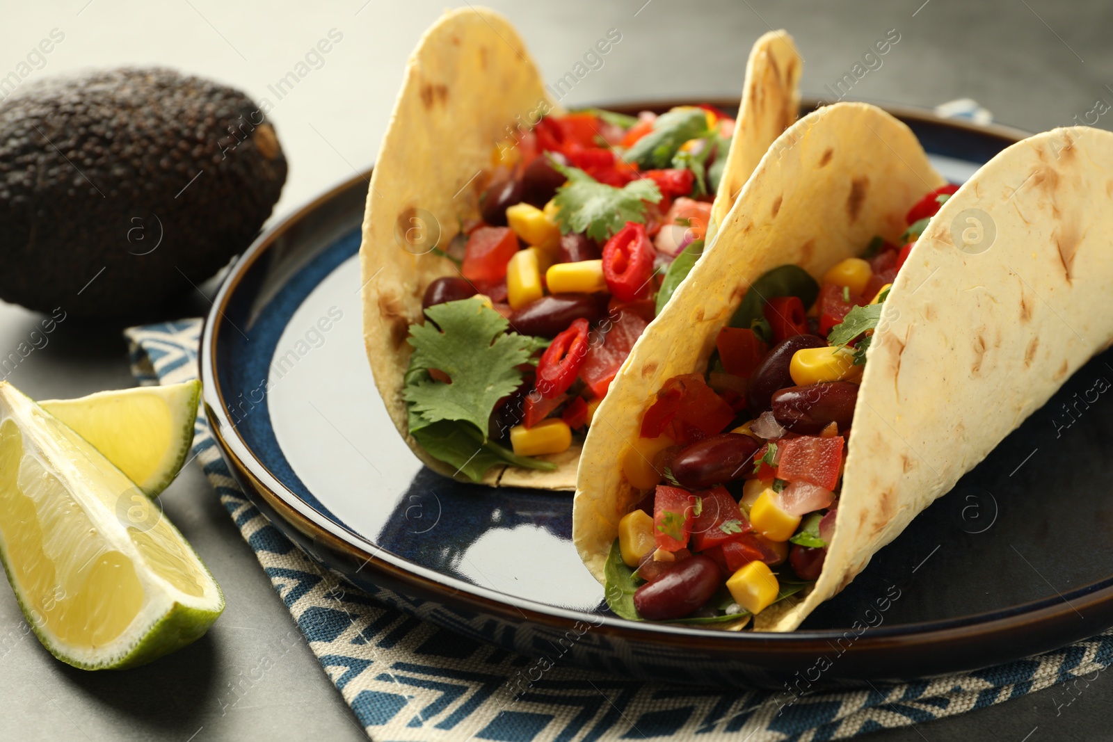 Photo of Tasty vegetarian tacos with beans, vegetables, avocado and lime on grey table, closeup