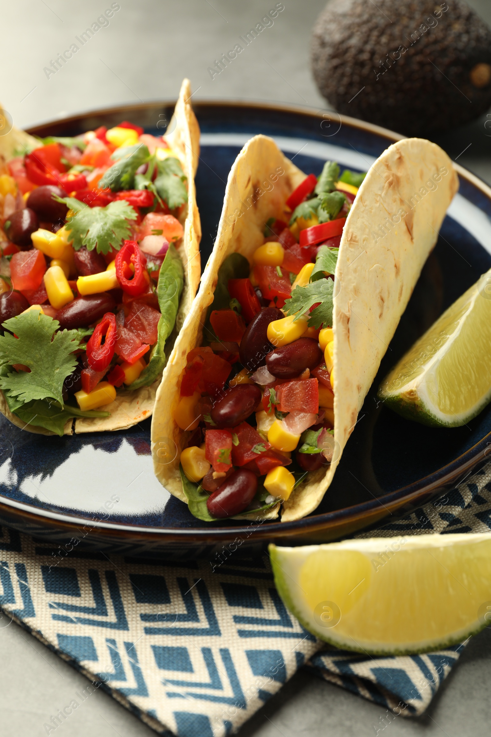 Photo of Tasty vegetarian tacos with beans, vegetables, avocado and lime on grey table, closeup