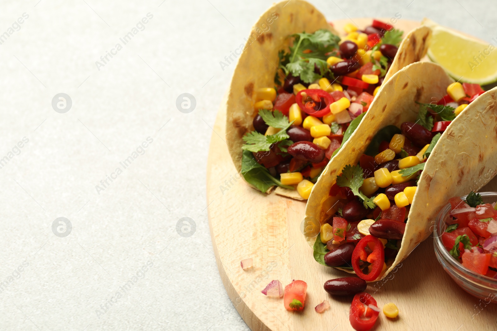 Photo of Tasty vegetarian tacos with beans, vegetables and lime on light grey table, closeup. Space for text