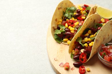 Photo of Tasty vegetarian tacos with beans, vegetables and lime on light grey table, closeup. Space for text