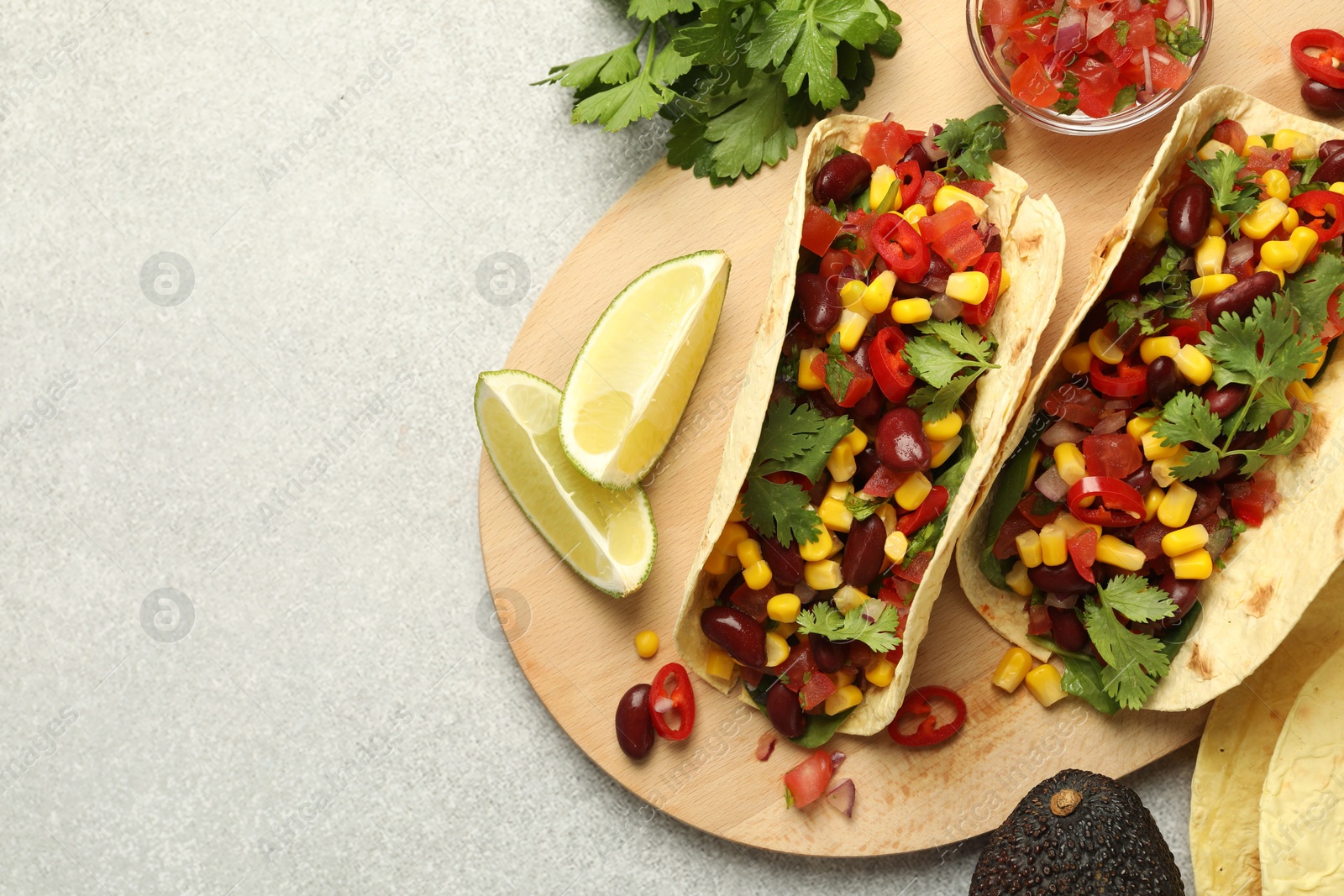 Photo of Tasty vegetarian tacos and ingredients on light grey table, flat lay. Space for text