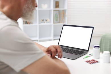 Photo of Senior man having online consultation with doctor via laptop at table indoors, closeup
