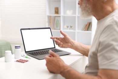Photo of Senior man having online consultation with doctor via laptop at table indoors, closeup