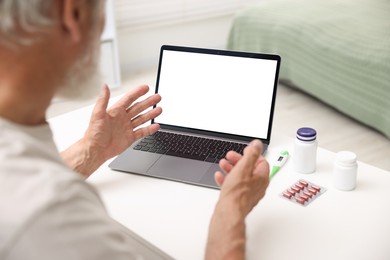 Photo of Senior man having online consultation with doctor via laptop at table indoors, closeup