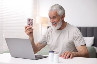 Photo of Senior man with pills having online consultation with doctor via laptop at table indoors