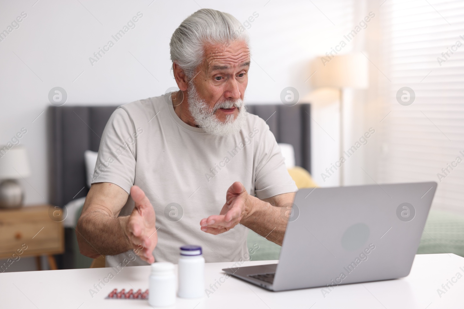 Photo of Senior man having online consultation with doctor via laptop at table indoors