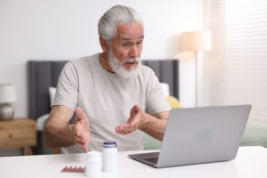 Photo of Senior man having online consultation with doctor via laptop at table indoors