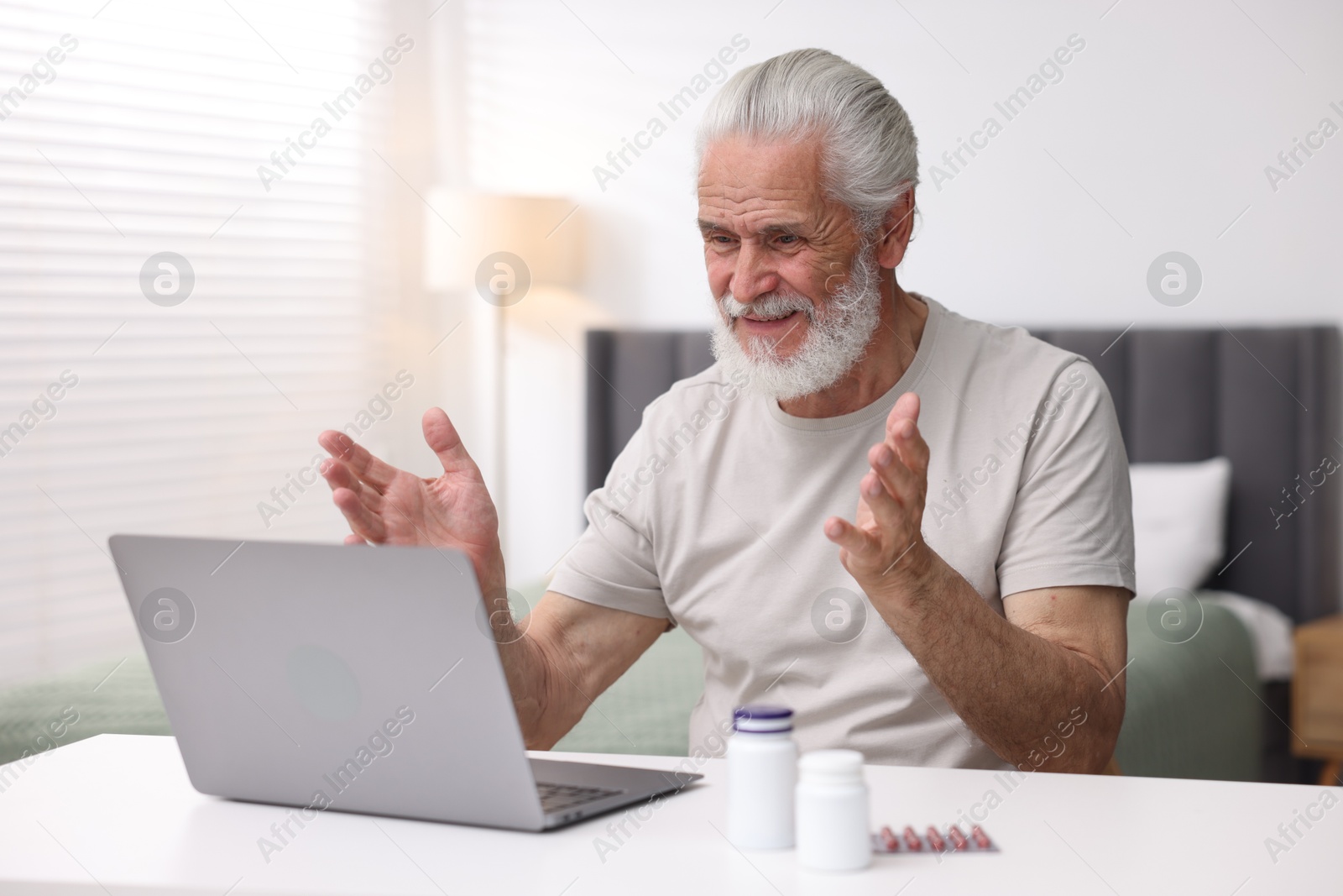 Senior man having online consultation with doctor via laptop at table indoors Photo of Senior man having online consultation with doctor via laptop at table indoors