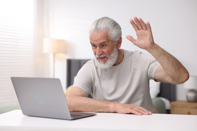 Photo of Senior man having online consultation with doctor via laptop at table indoors