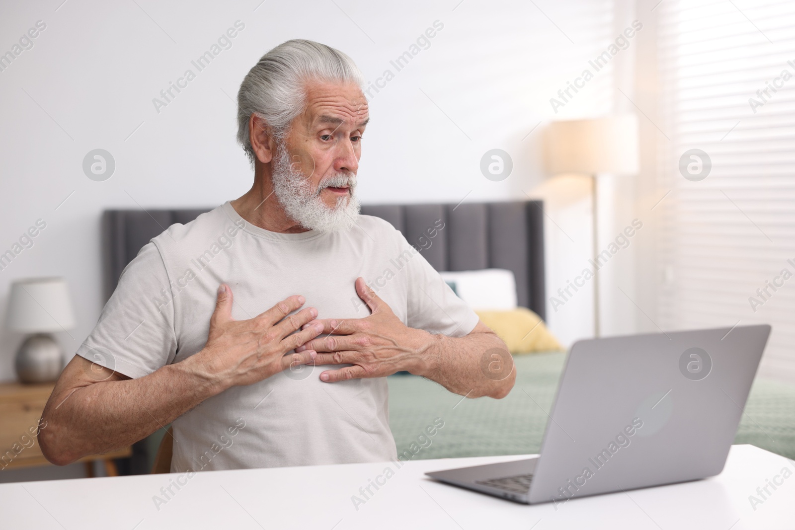 Photo of Senior man having online consultation with doctor via laptop at table indoors