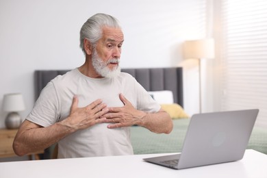 Photo of Senior man having online consultation with doctor via laptop at table indoors