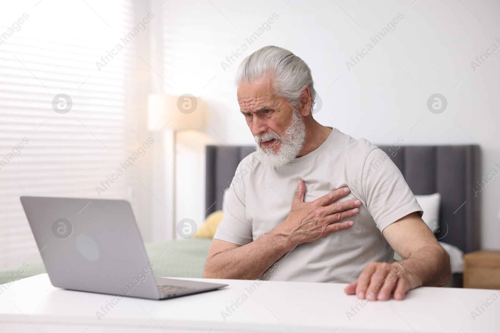 Senior man having online consultation with doctor via laptop at table indoors Photo of Senior man having online consultation with doctor via laptop at table indoors