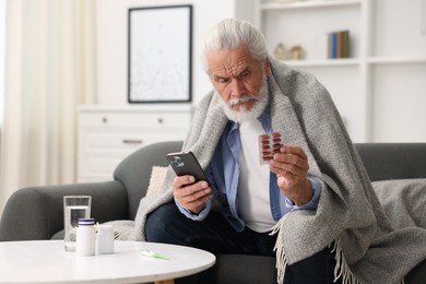 Photo of Senior man with pills having online consultation with doctor via smartphone at home