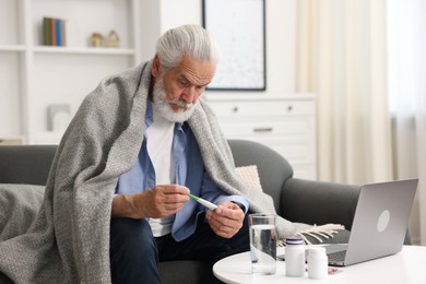 Photo of Senior man with thermometer having online consultation with doctor via laptop at home