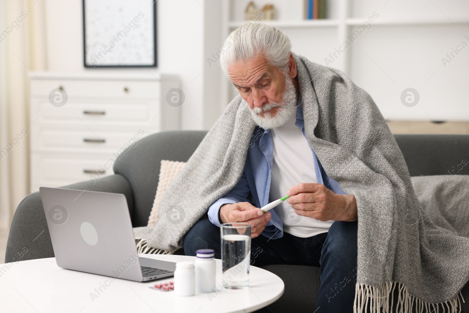 Senior man with thermometer having online consultation with doctor via laptop at home Photo of Senior man with thermometer having online consultation with doctor via laptop at home