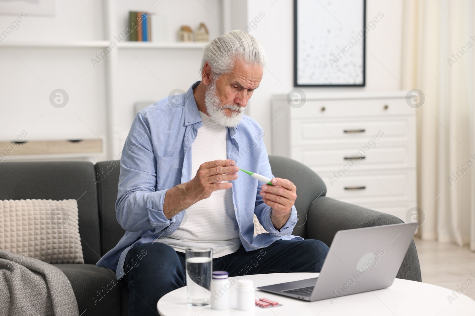 Senior man with thermometer having online consultation with doctor via laptop at home Photo of Senior man with thermometer having online consultation with doctor via laptop at home