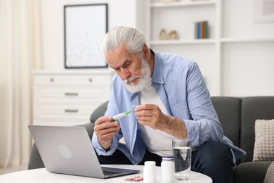 Photo of Senior man with thermometer having online consultation with doctor via laptop at home