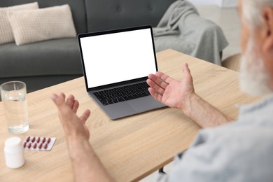 Photo of Senior man having online consultation with doctor via laptop at table indoors, closeup
