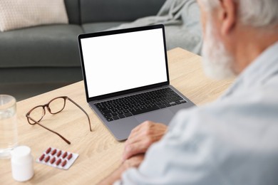 Photo of Senior man having online consultation with doctor via laptop at table indoors, closeup