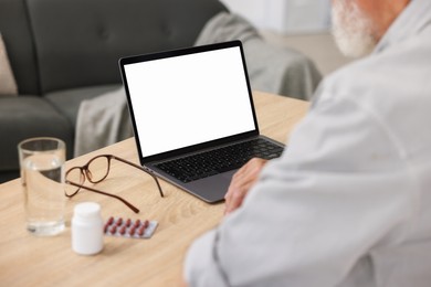 Photo of Senior man having online consultation with doctor via laptop at table indoors, closeup