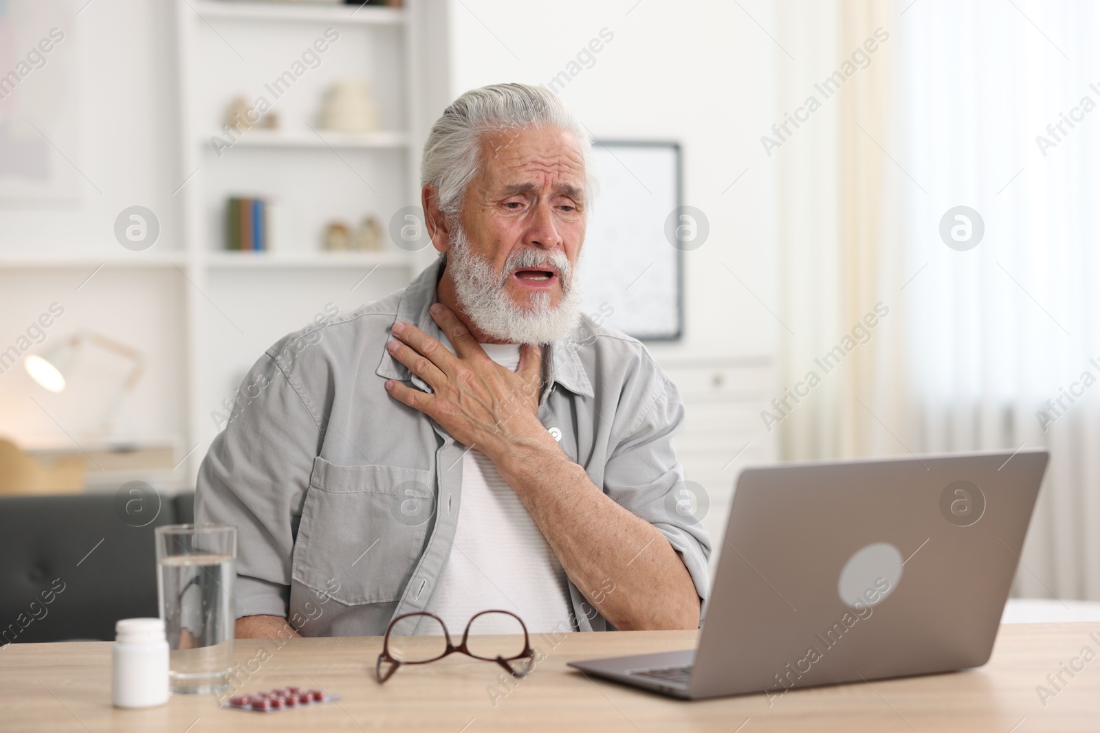 Photo of Senior man having online consultation with doctor via laptop at table indoors