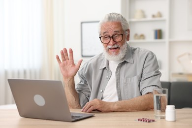 Photo of Senior man having online consultation with doctor via laptop at table indoors