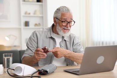 Photo of Senior man with pills having online consultation with doctor via laptop at table indoors