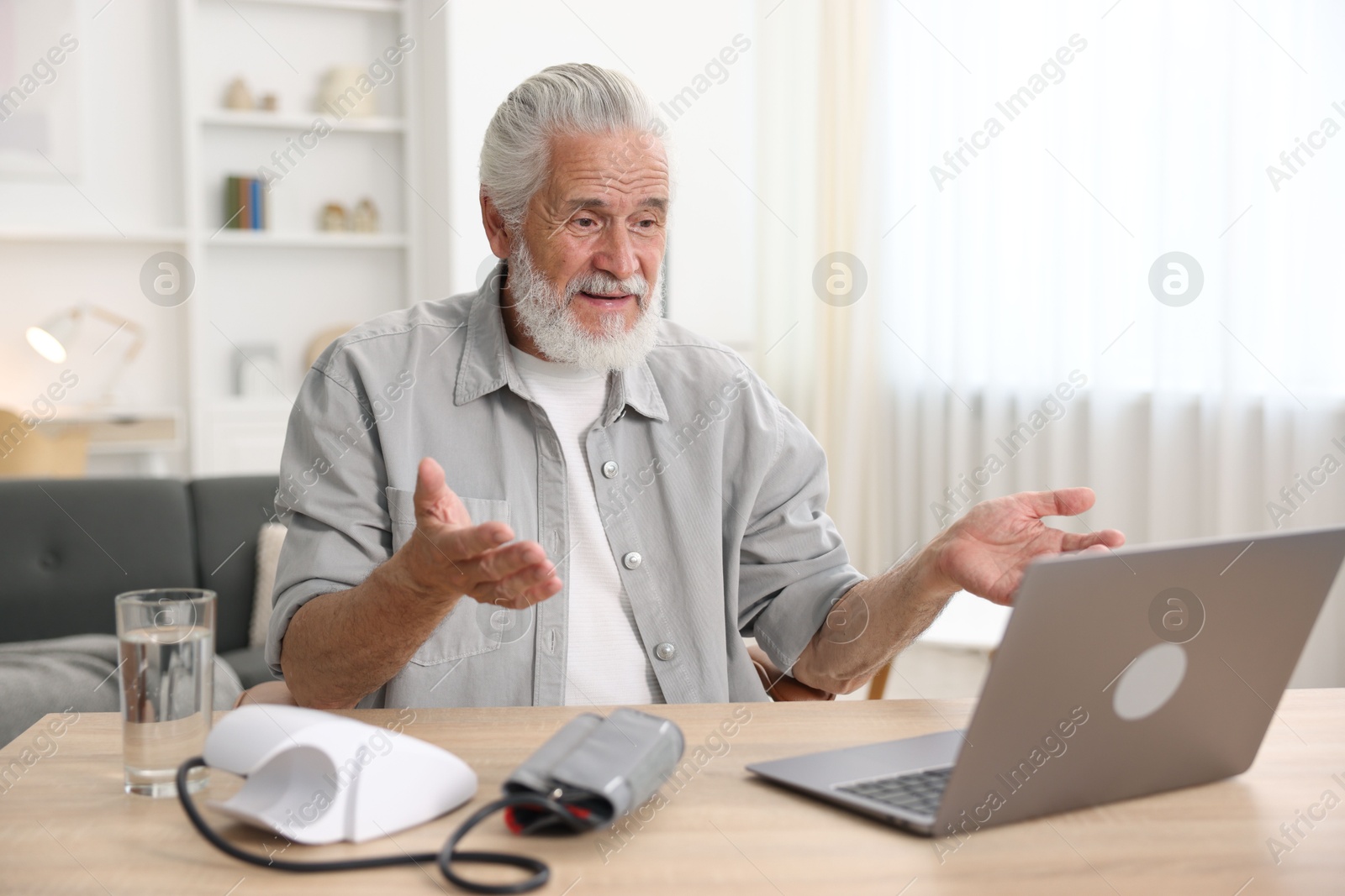 Photo of Senior man having online consultation with doctor via laptop at table indoors