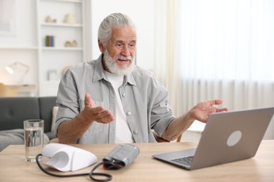 Photo of Senior man having online consultation with doctor via laptop at table indoors