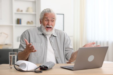 Photo of Senior man having online consultation with doctor via laptop at table indoors